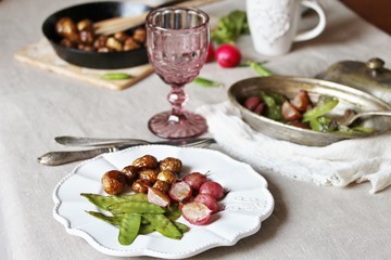 young summer vegetables-fried radish, young peas and young potatoes. dinner served at the table, beautiful table setting.