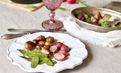 young summer vegetables-fried radish, young peas and young potatoes. dinner served at the table, beautiful table setting.
