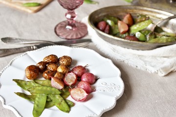 young summer vegetables-fried radish, young peas and young potatoes. dinner served at the table, beautiful table setting.