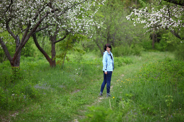 Fototapeta na wymiar Beautiful mature woman posing for the camera in the spring garden. The girl enjoys the flowering of apple trees.