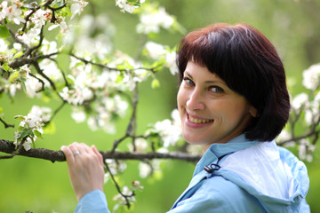 Obraz premium Beautiful mature woman posing for the camera in the spring garden. The girl enjoys the flowering of apple trees.