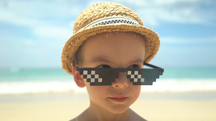 portrait of cute little boy in straw hat with sunglasses standing on summer beach