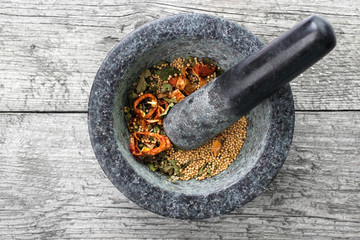 Granite mortal with dried herbs on gray wooden surface , top view