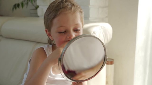 a small boy with blond hair with mirror opening his mouth to show where he lost one of his baby's teeth