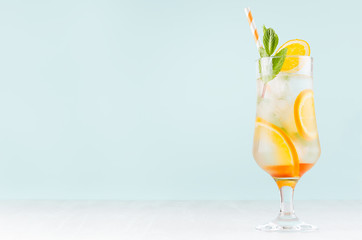 Fresh orange cocktail with slices fruits, mint, straw, ice cubes in misted glass on white wood table and blue color wall, copy space.