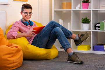 Modern student in glasses sitting on beanbag chair reading e-book
