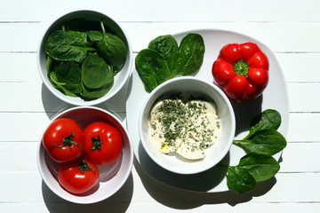 Spinach, tomatoes, mozzarella and a bell pepper on white plates and bowls