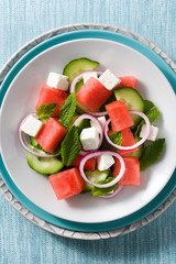 watermelon salad with feta cheese,mint,onion and cucumber on blue background. Close up