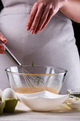 young woman in a gray aprons breaks the eggs