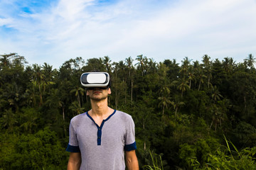 Young man with VR glasses in the tropical forest