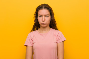 Fototapeta premium Young european woman isolated over yellow background blows cheeks, has tired expression. Facial expression concept.