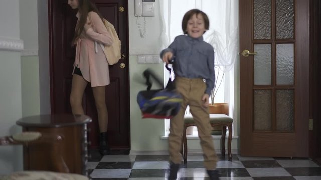 Young girl and little brother with backpack entering the house. Children are happy to back home, boy is smiling. Kids as adults