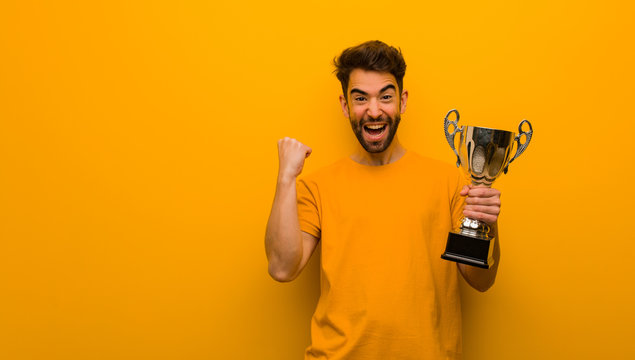 Young man holding a trophy surprised and shocked