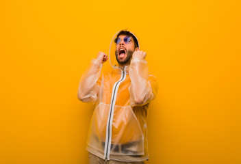Young man wearing a rain coat screaming very angry and aggressive © Asier