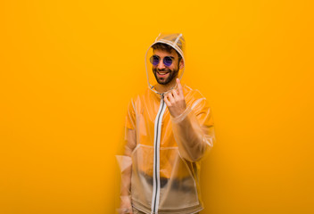 Young man wearing a rain coat inviting to come