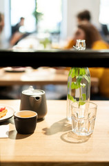 Gray teapot on a wooden table in a cafe. Black mug for tea. Dessert on a white plate and sliced lemon on a small saucer. Glass for water and a carafe.