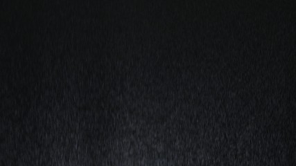 4k Heavy angled rain falling in front of the camera against black screen. Raindrops splashing. Rain closeup vfx insert. Practical seamlessly loopable footage. Heavy rainstorm hitting black surface.