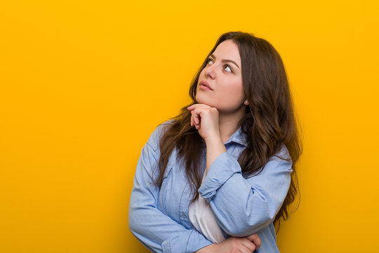 Young curvy plus size woman looking sideways with doubtful and skeptical expression.