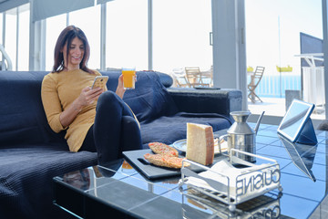 Una mujer joven desayuna en un día soleado en el sofá de su casa