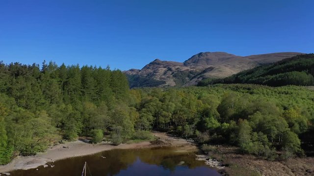 Dolly shot above Loch Lomond towards Ben Lomond, Mountain with secluded yacht and forest.