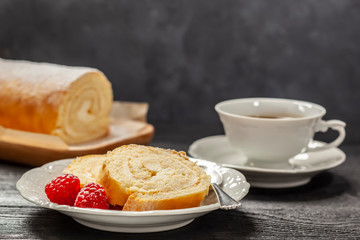 Ciasto - rolada biszkoptowa z kremem mascarpone na talerzyku, obok kawa w filiżance, wszystko postawione na czarnym drewnianym blacie © Grzej