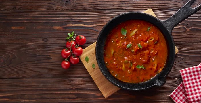Cooking pasta penne with tomato sauce and basil on iron cast pan. Wooden table, top view