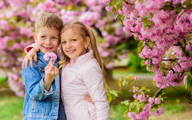 Romantic babies. Kids enjoying pink cherry blossom. Tender love feelings. Couple kids on flowers of sakura tree background. Little girl enjoy spring flowers. Giving all flowers to her. Surprising her