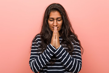 Young intellectual indian woman holding hands in pray near mouth, feels confident.