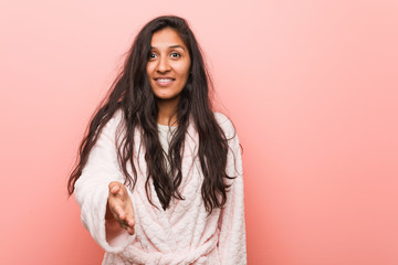 Fototapeta premium Young indian woman wearing pajama stretching hand at camera in greeting gesture.