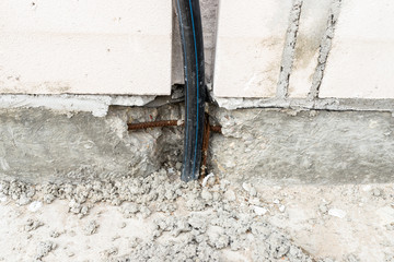 An electric high voltage cable protruding from the foundation of the house being built.