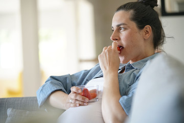 Pregnant woman relaxing at home, eating strawberries