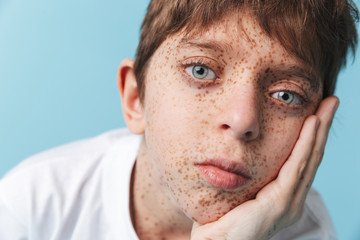 Portrait closeup of sad beautiful boy 10-12y with freckles wearing white casual t-shirt looking at camera