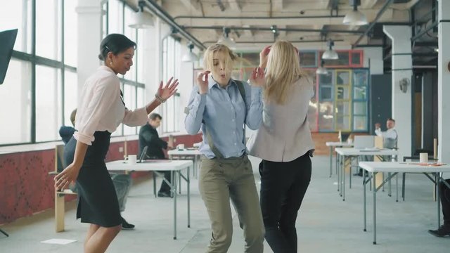 Women colleagues dancing together. Office workers celebrate and dance. Creative office interior in the style of a loft. Coworking