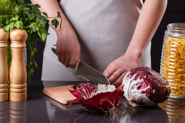 young woman in a gray aprons cuts radicchio