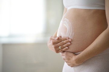Pregnant woman applying stretch mark removal lotion on her belly - obrazy, fototapety, plakaty