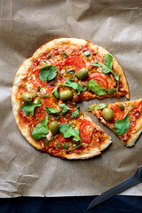 Homemade vegetarian pizza with tomato sauce, two types of cheese, tomatoes, peppers, arugula, olives and herbs. Top view.