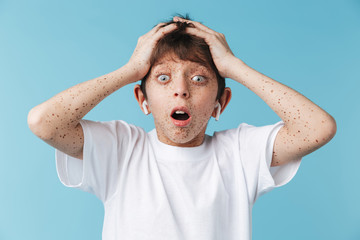 Image closeup of excited caucasian boy 10-12y with freckles wearing white casual t-shirt and earpods screaming at camera