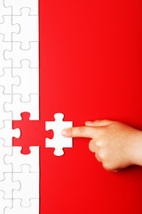 Children's hand moves a piece of white puzzle on a red background