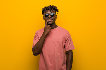 Young casual black man wearing sunglasses looking sideways with doubtful and skeptical expression.