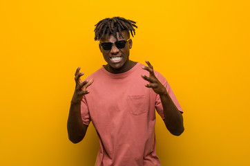 Young casual black man wearing sunglasses upset screaming with tense hands.