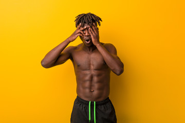 Fototapeta premium Young black man shirtless wearing swimsuit blink through fingers frightened and nervous.