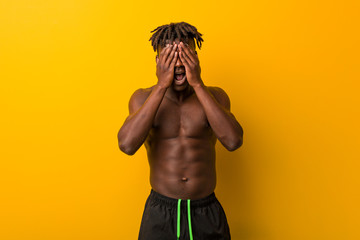 Young black man shirtless wearing swimsuit covers eyes with hands, smiles broadly waiting for a surprise.