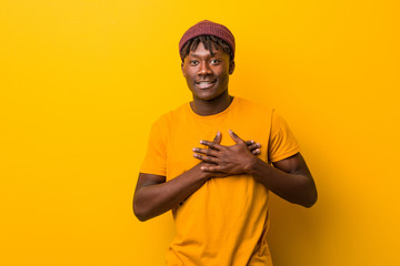 Fototapeta na wymiar Young black man wearing rastas over yellow background has friendly expression, pressing palm to chest. Love concept.