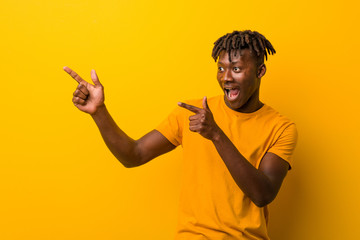 Young black man wearing rastas over yellow background pointing with forefingers to a copy space,...