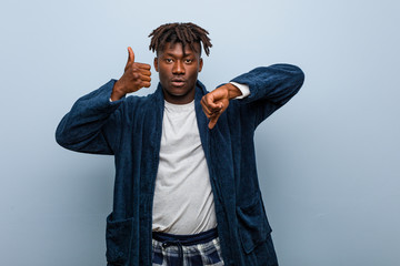 Young african black man wearing pajama showing thumbs up and thumbs down, difficult choose concept
