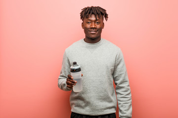 Young fitness black man holding a water bottle happy, smiling and cheerful.