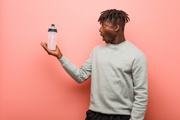 Young fitness black man holding a water bottle impressed holding copy space on palm.