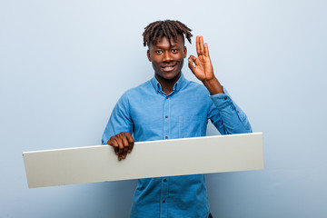 Young rasta black man holding a placard cheerful and confident showing ok gesture.