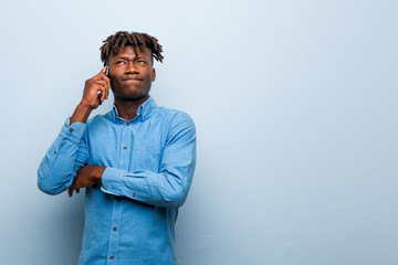 Young rasta black man holding a phone smiling confident with crossed arms.