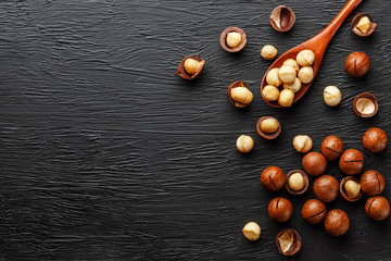Shelled macadamia nut and peeled macadamia nut on a black textural background in a wooden spoon